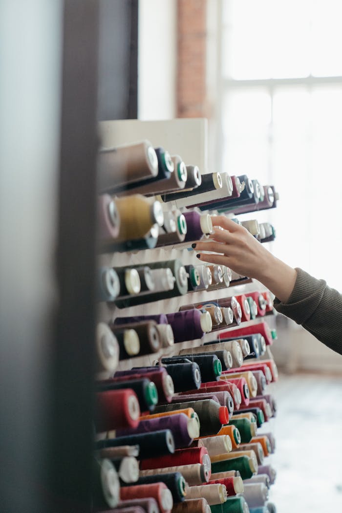 A hand reaches for spools of colorful sewing thread in a well-lit workshop, showcasing variety and organization.