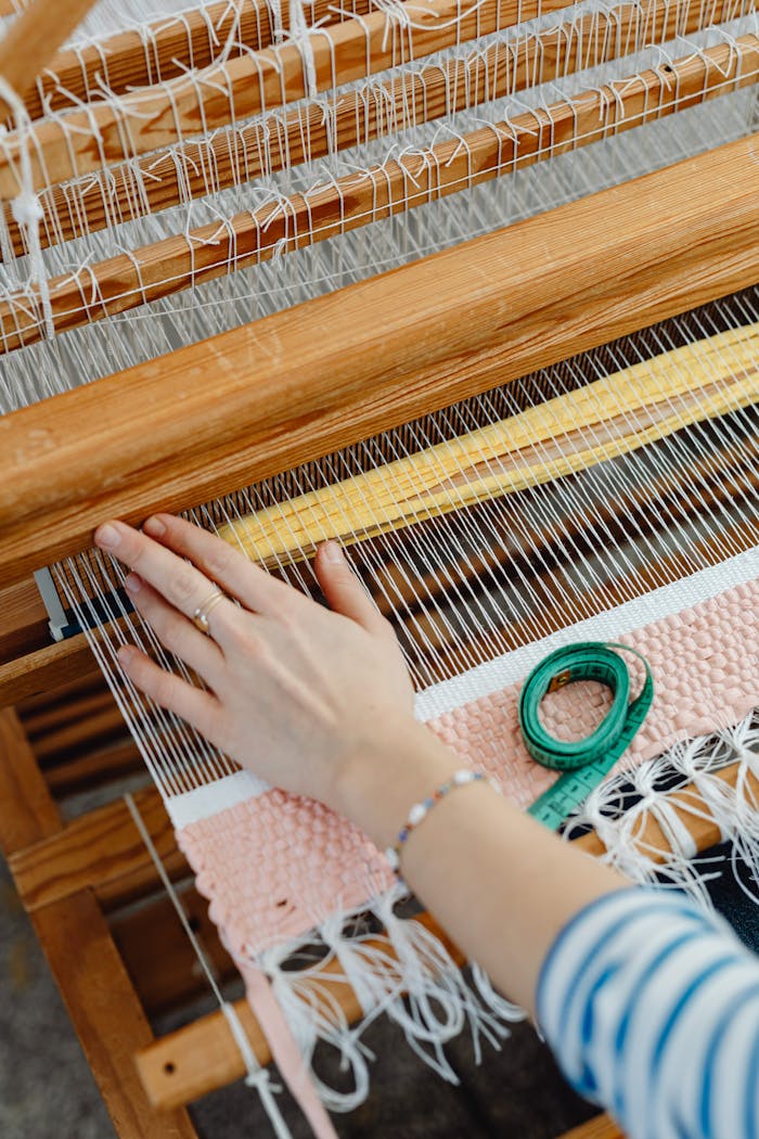 A hand weaving colorful threads on a wooden loom, highlighting craftsmanship.
